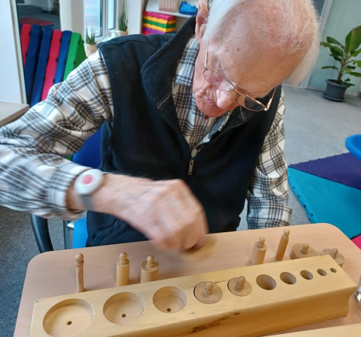 Ein Senior setzt Zylinder in einen Montessori-Einsatzblock