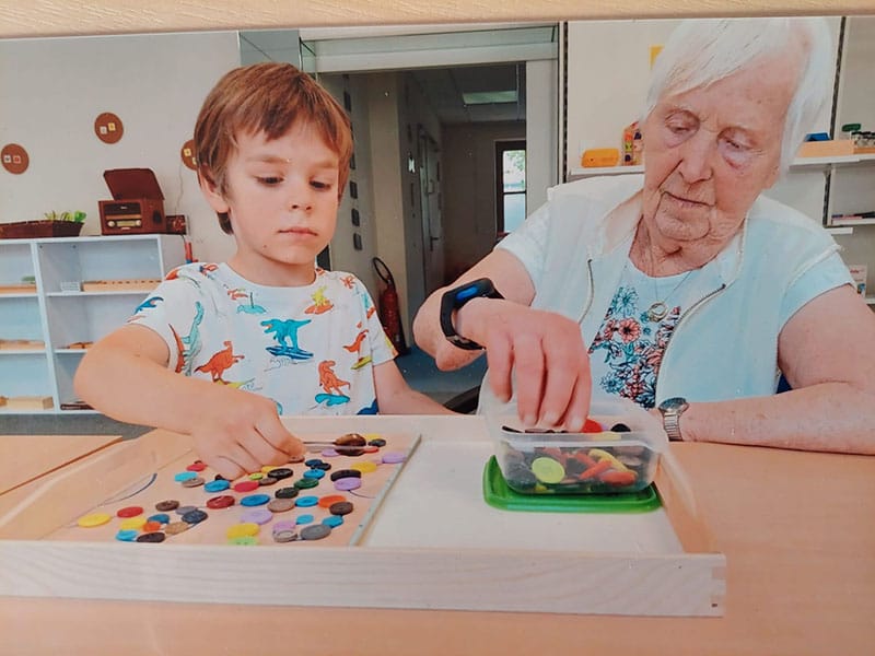 Ein Kind und eine Seniorin arbeiten nebeneinander mit Legematerial